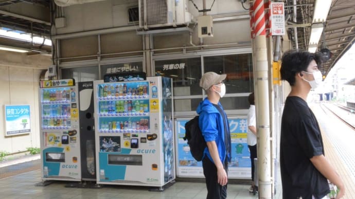 ベンディングマシン背後のホーム内駅務室のガラス窓に「環境にやさしい、列車の旅」の記載、、【中央線ホーム内:中央快速線】 2022.AUG