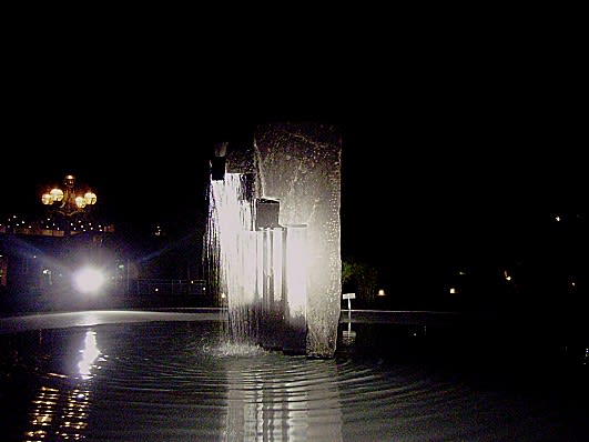 夜、池の中にある石の柱のようなオブジェから滝のように水が流れ落ちている