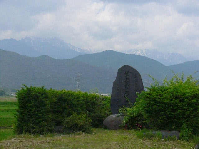遠くに北アルプスの峰。石碑に景観讃美「望岳豊穣之地」の文字が刻まれている