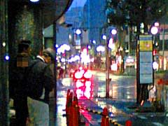 雨の中、多摩信用金庫のビル影で雨宿りする乗客達